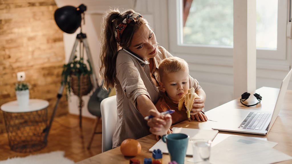 mulher, mãe, a segurar um bebé enquanto está ao telefone, a trabalhar e a alimentar o filho. Mulher atarefada em multitasking.
