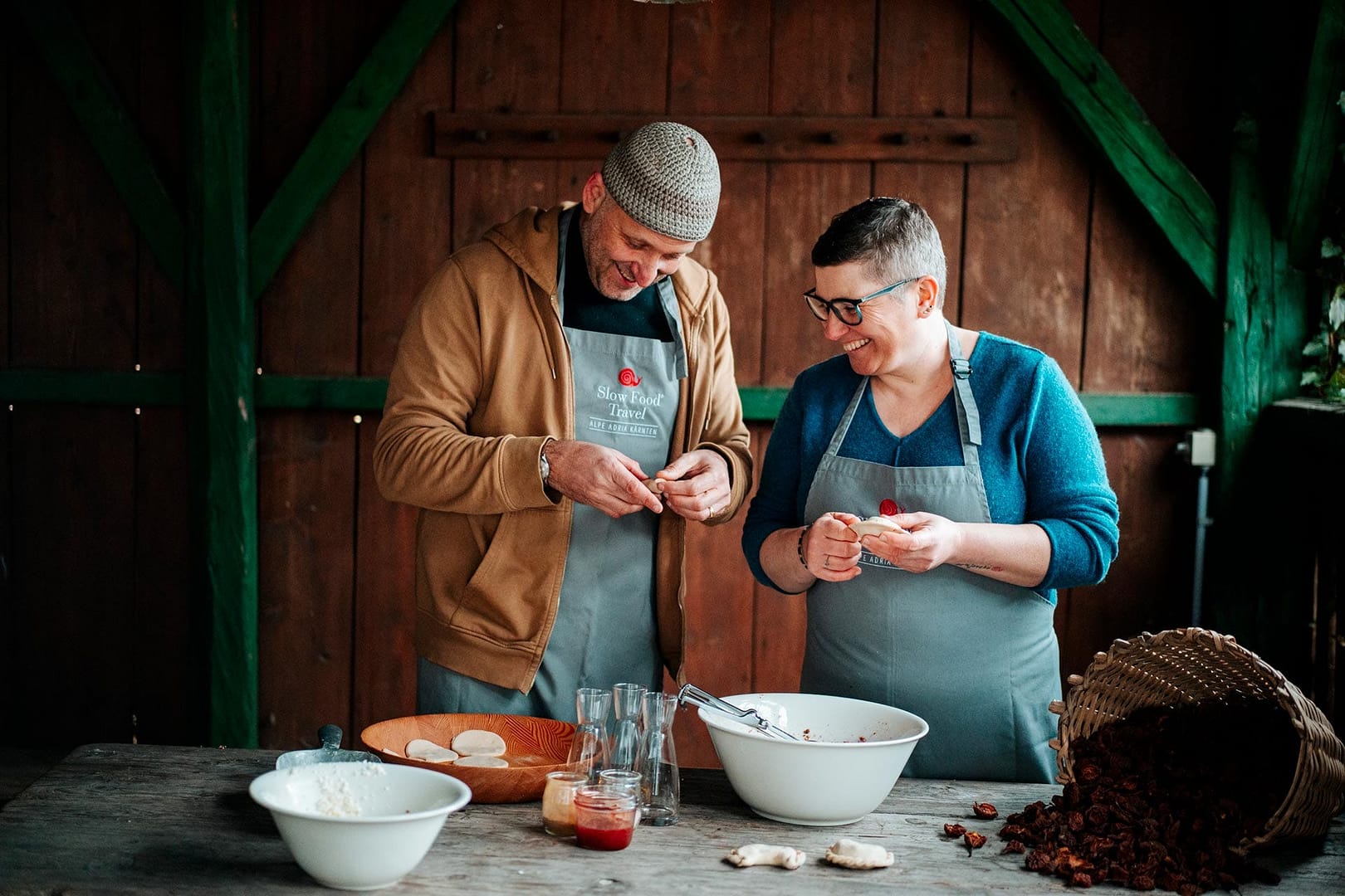 dois membros da assocuiação Slow Food, sorridentes, a cozinhar com produtos locais e sustentáveis.