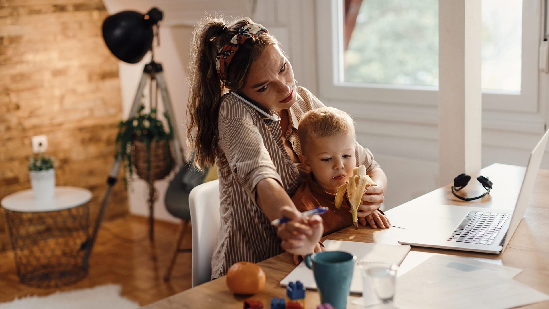 mulher, mãe, a segurar um bebé enquanto está ao telefone, a trabalhar e a alimentar o filho. Mulher atarefada em multitasking.