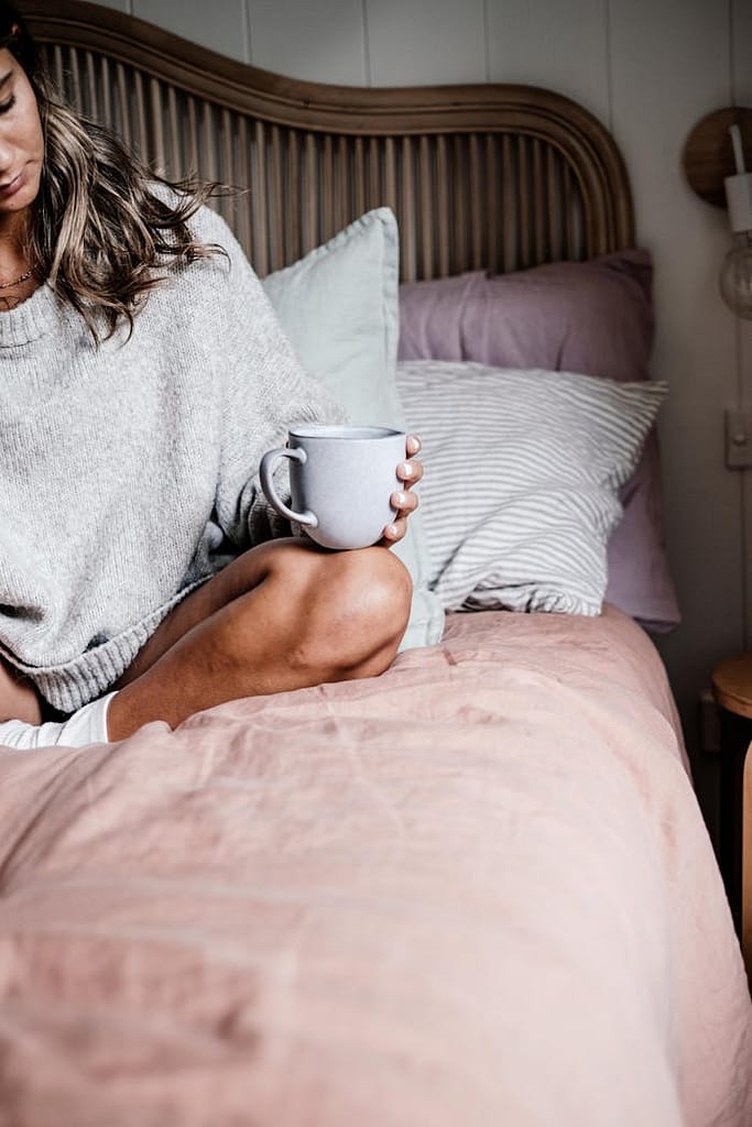 Mulher jovem a viver devagar, sentada na cama com uma caneca nas mãos, num ambiente tranquilo e minimalista — símbolo do estilo de vida slow living.